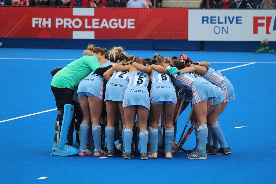 female Argentinian field hockey players wearing blue jerseys in a huddling position
