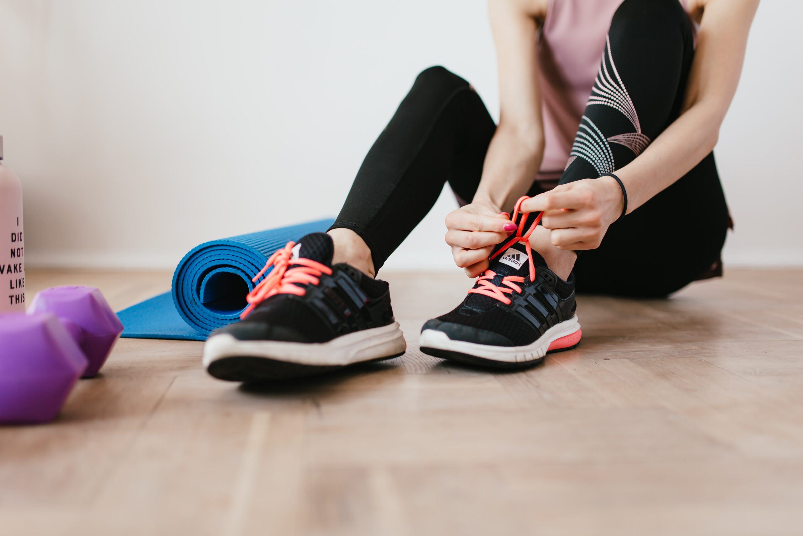 anonymous slender female athlete tying shoelace near sports accessories 