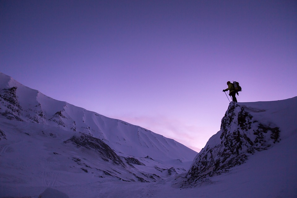 A man with a backpack standing at the edge of a cliff covered with snow