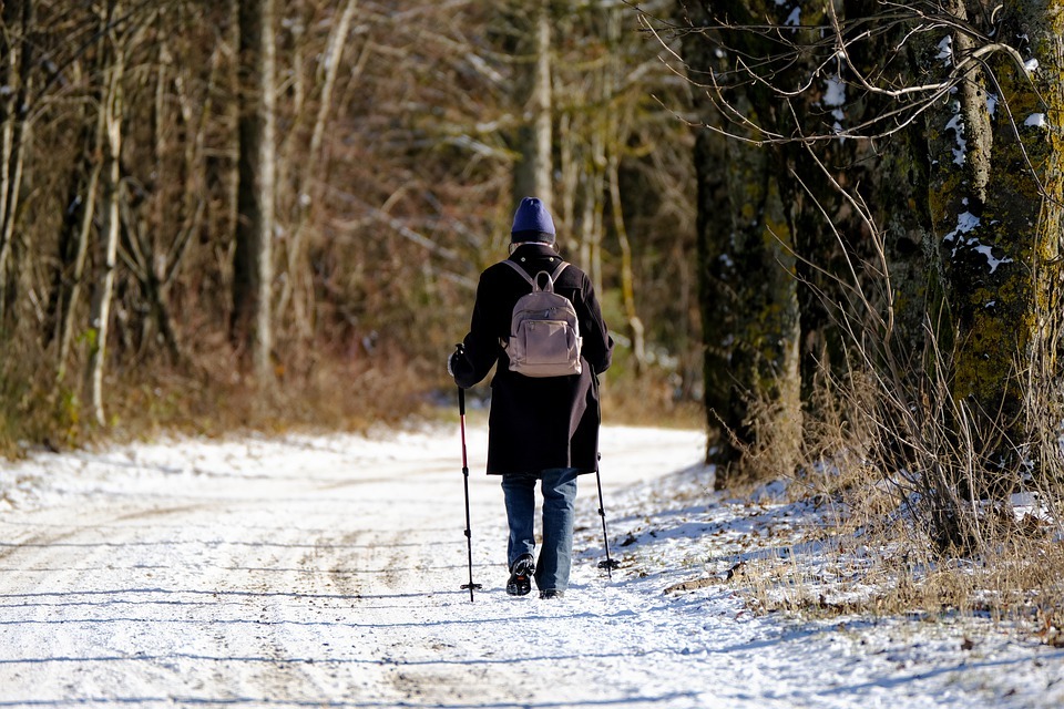 An old woman in winter jacket, with a backpack, walking on a road with snow