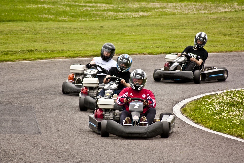a racetrack, green field, four go-kart racers, go-karts, helmets