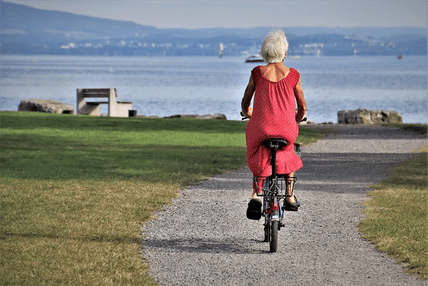 an old woman in a red dress cycling on a concrete road beside the sea