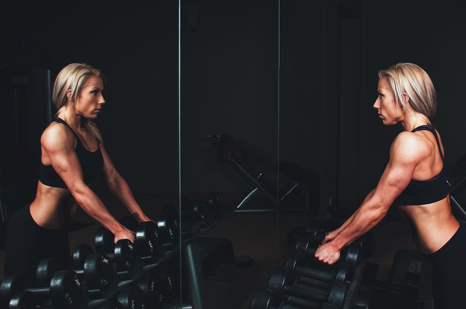 blonde girl with muscles working out, black dumbbells in line, mirror with the reflection of the girl