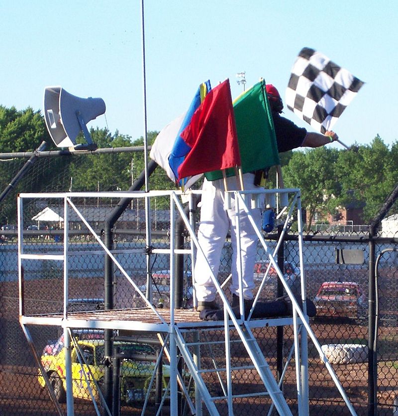 flagman displaying the checkered flag with a complete set of racing flags