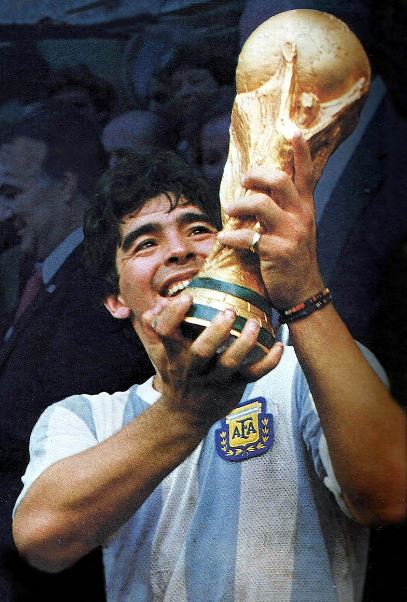 Diego Maradona smiling while holding and looking up at the trophy